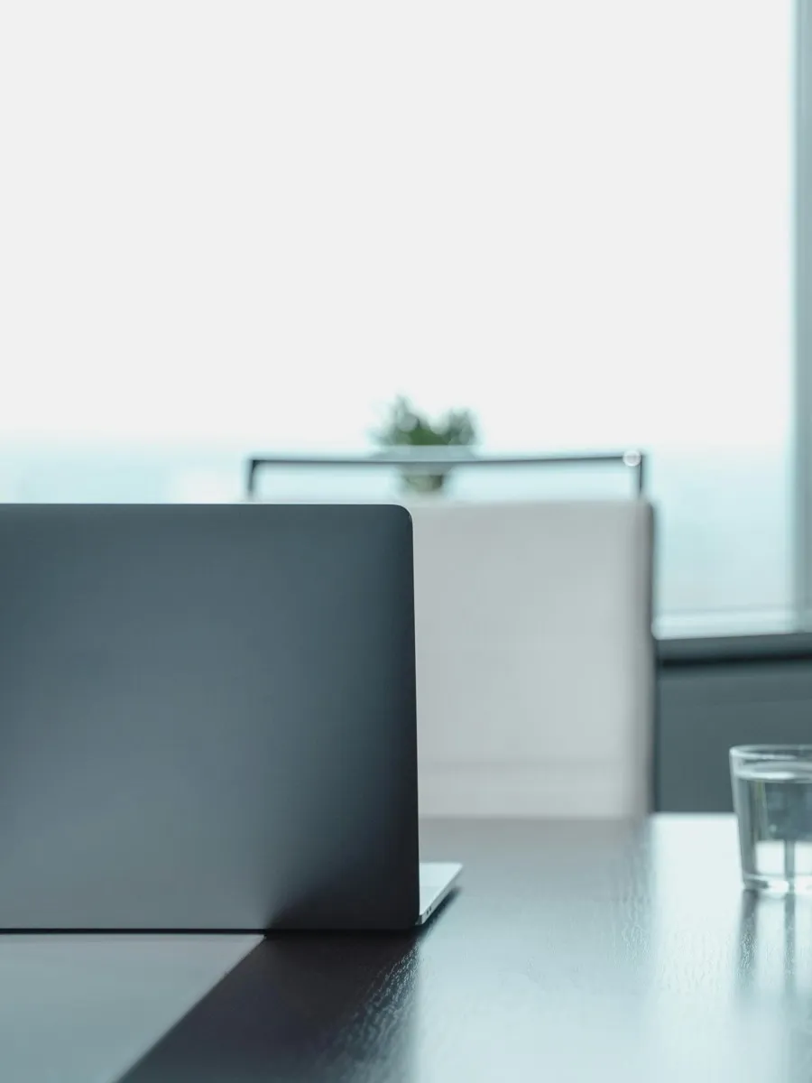 Thomas Uder Vermögensberatung – Laptop und Wasserglas auf einem Tisch am Fenster in einem hellen Büro